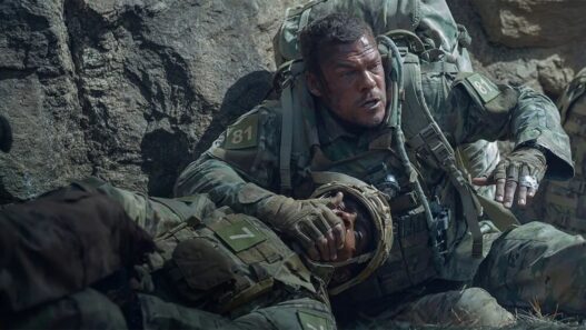 Alan Ritchson vestido de militar y tapando a otro soldado con la mano en una escena de la película Máquina de Hierro que triunfa en Netflix.
