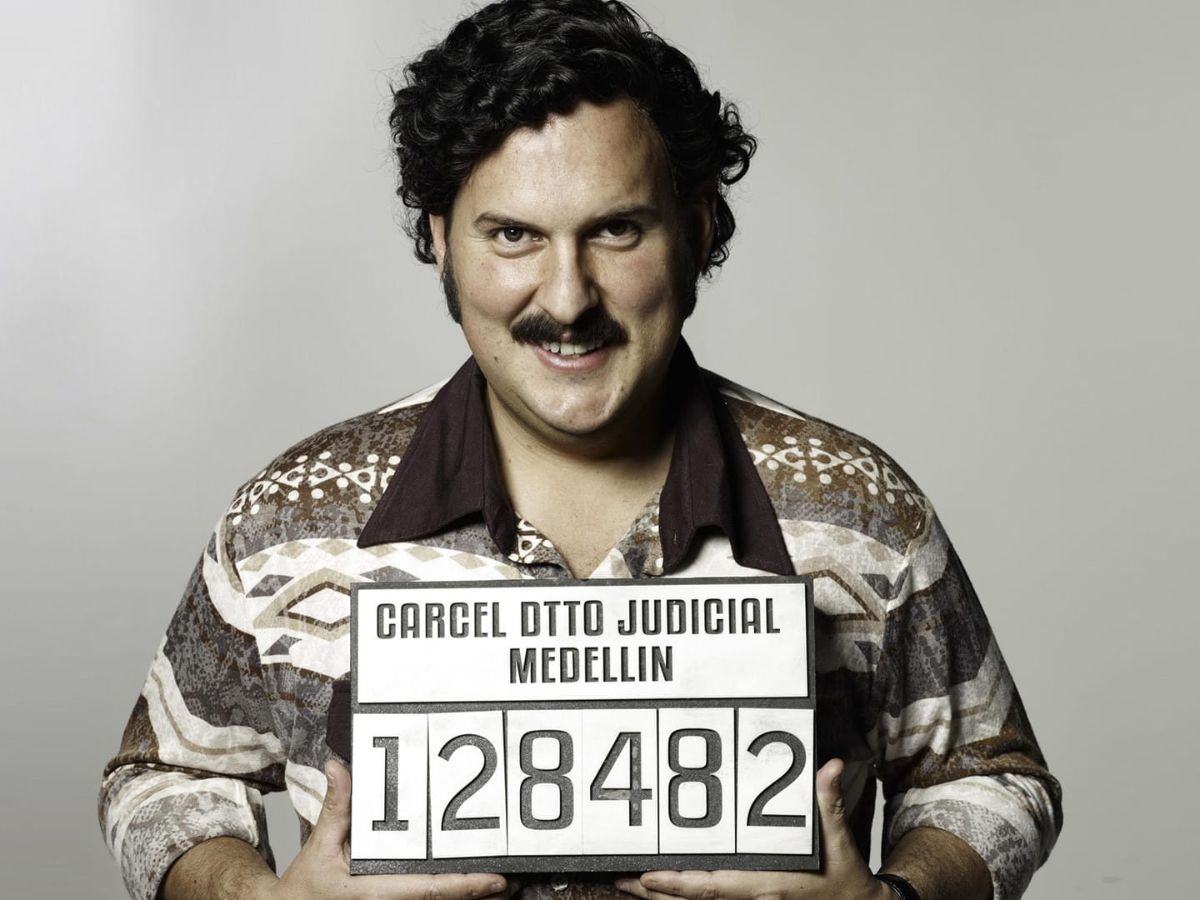 El actor Andrés Parra sujetando un cartel de su ficha en comisaría en la serie Pablo Escobar: el patrón del mal.