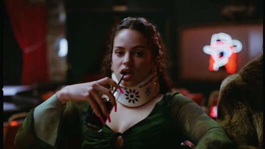 Rosalía con un collarín y bebiendo un refresco con pajita interpretando a Magick, una bailarina de pole dance en Euphoria.