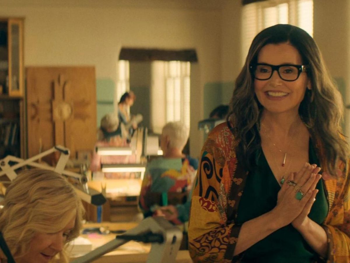 Primer plano de Geena Davis con gafas y sonriendo en una escena en una residencia de mayores en la serie The Boroughs: jubilación rebelde.