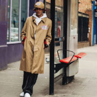 Cómo vestir para un día de lluvia: 5 looks con trench y gabardina para presumir de estilo bajo el paraguas Hombre vestido con una gabardina beige y un sombrero apoyado en una parada de autobús en la calle