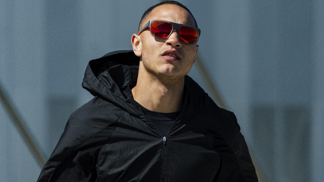 Hombre con chaqueta negra con capucha y gafas Mó Sport Fiber de lentes espejadas rojas mirando al horizonte