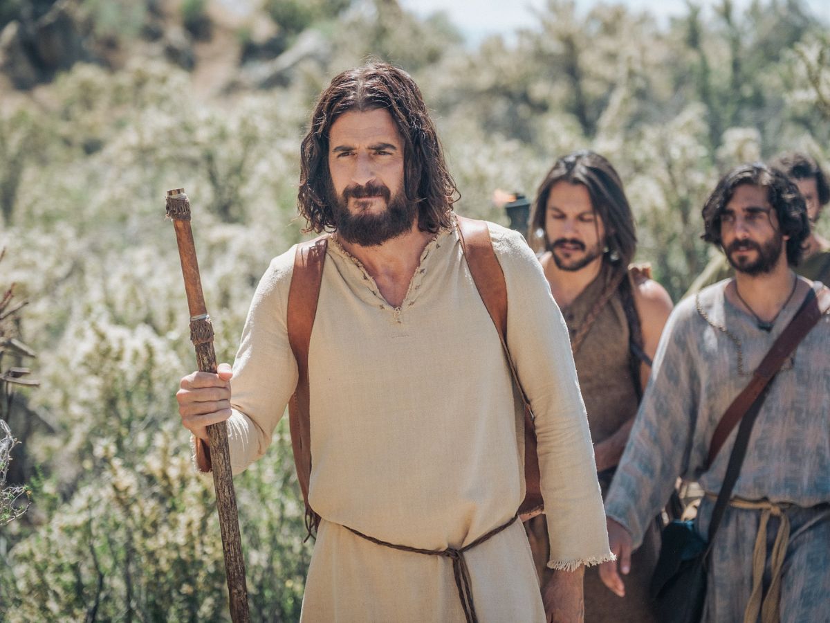 Jonathan Roumie como Jesús con túnica beige y un bastón en la mano derecha guiando al pueblo en la serie The Chosen.