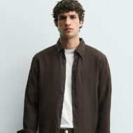 Zara tiene las 5 camisas de lino en color chocolate que prometen agotarse antes de mayo modelo vestido con una camisa de lino marrón y una camiseta básica de Zara primavera 2026