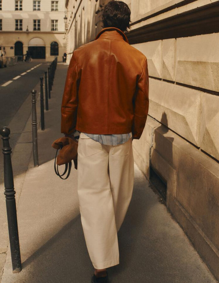 Look de hombre Zara con pantalones anchos blancos cazadora de piel camel sandalias de tiras y bolso.