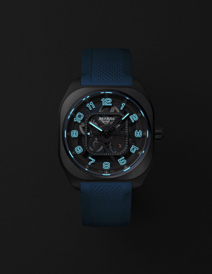 Hermès H08 Squelette 2026 en la oscuridad con índices y agujas iluminados en azul eléctrico por el Super-LumiNova