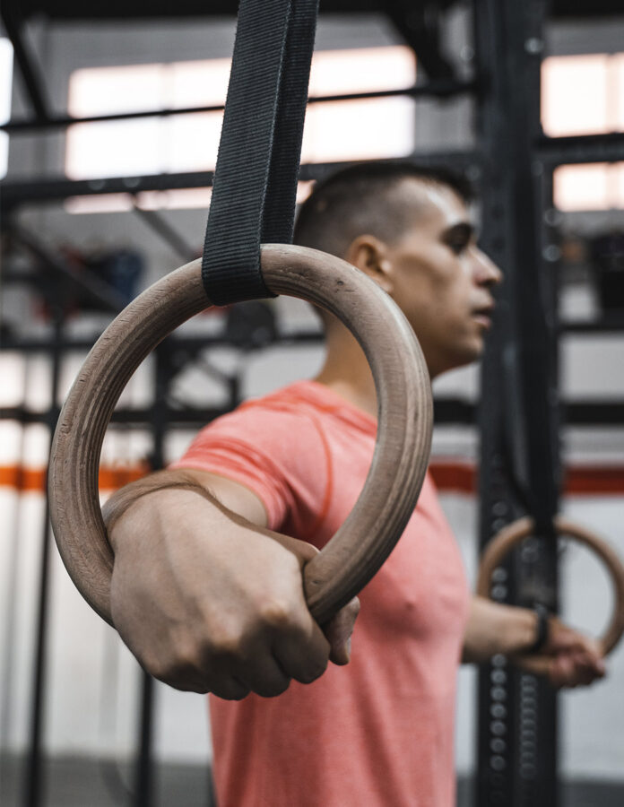 Adrián Sandoya sujeta unas anillas de madera en el gimnasio, material utilizado para entrenar tracciones horizontales como el remo invertido.