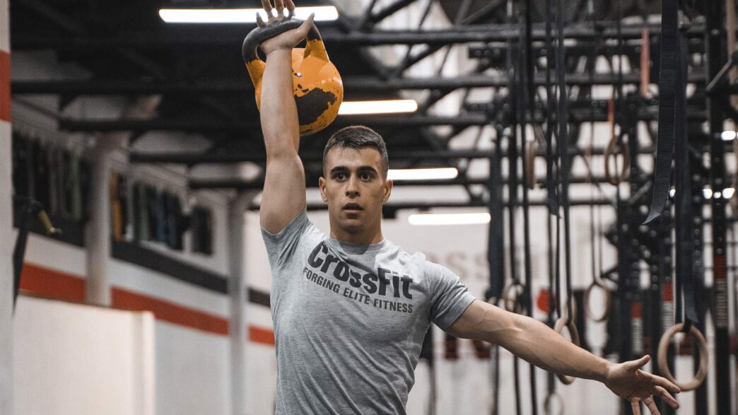 Adrián Sandoya, entrenador personal, sostiene una kettlebell sobre la cabeza durante un entrenamiento de alta intensidad en el gimnasio.
