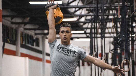 Adrián Sandoya, entrenador personal, sostiene una kettlebell sobre la cabeza durante un entrenamiento de alta intensidad en el gimnasio.