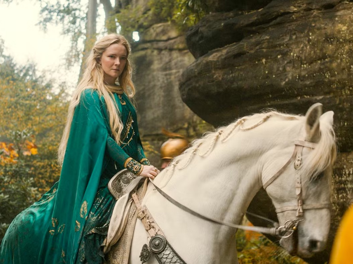 Galadriel cabalga sobre un caballo blanco vestida con una capa verde esmeralda en un bosque de 'Los anillos del poder'.