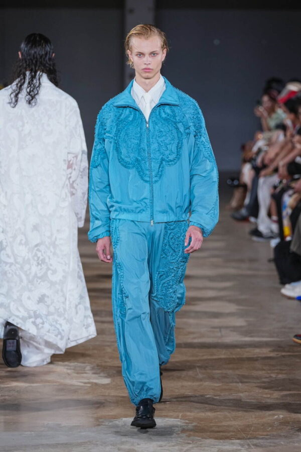 Conjunto en azul saturado turquesa de Taakk primavera/verano 2026 con apliques bordados sobre chaqueta y pantalón, y camisa blanca asomando bajo la cremallera