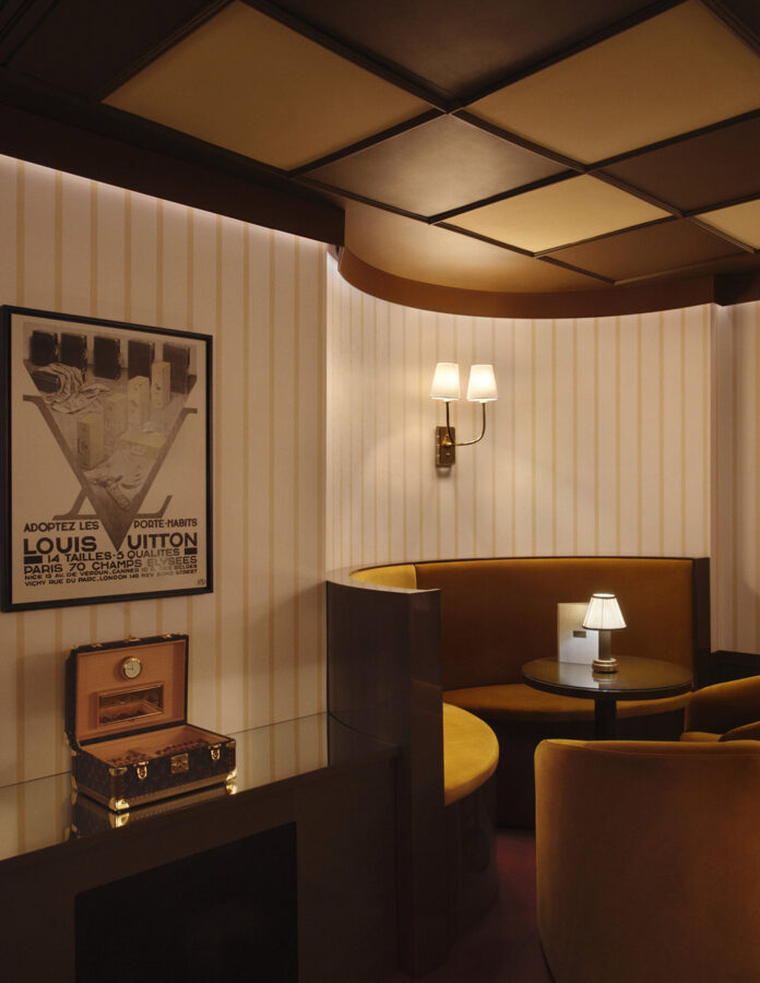 Bar Noé del Louis Vuitton Hotel London con cartel vintage de Louis Vuitton, sofás de terciopelo mostaza y baúl Monogram expuesto