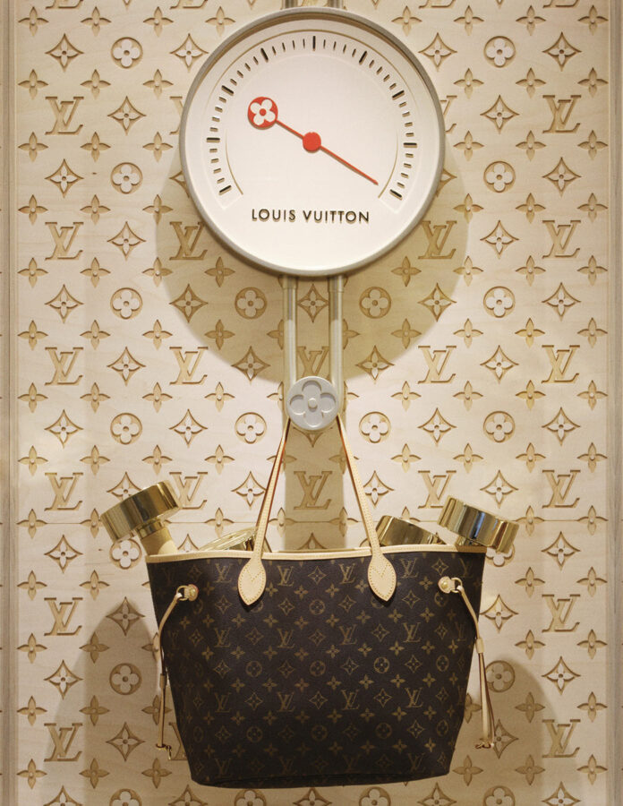 Bolso Neverfull de Louis Vuitton en lona Monogram con cuatro botellas de champán bajo una báscula clásica de la firma