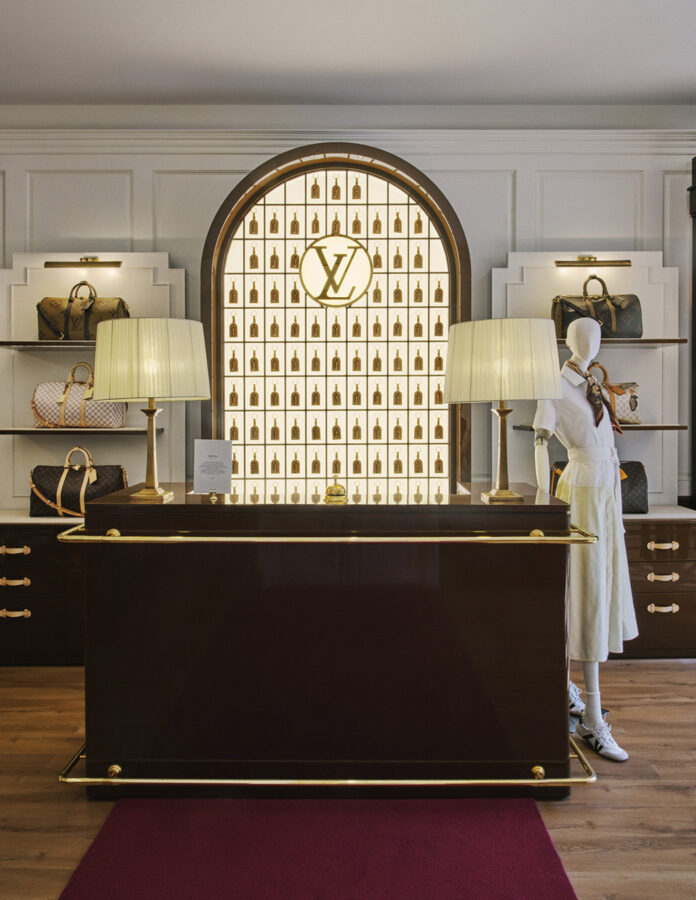 Recepción Keepall Lobby del Louis Vuitton Hotel London con mostrador de baúl, llaveros dorados y bolsos Keepall en estanterías