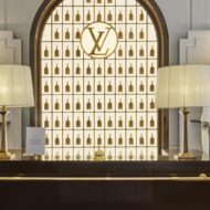 Louis Vuitton abre un hotel en Londres por tiempo limitado: así es por dentro y solo estará dos meses Mostrador del Keepall Lobby del Louis Vuitton Hotel London con maniquí vestido de blanco, lámparas de pantalla plisada y bolsos Keepall