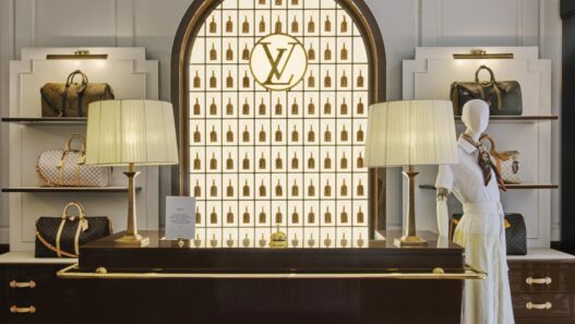 Mostrador del Keepall Lobby del Louis Vuitton Hotel London con maniquí vestido de blanco, lámparas de pantalla plisada y bolsos Keepall