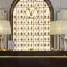 Mostrador del Keepall Lobby del Louis Vuitton Hotel London con maniquí vestido de blanco, lámparas de pantalla plisada y bolsos Keepall
