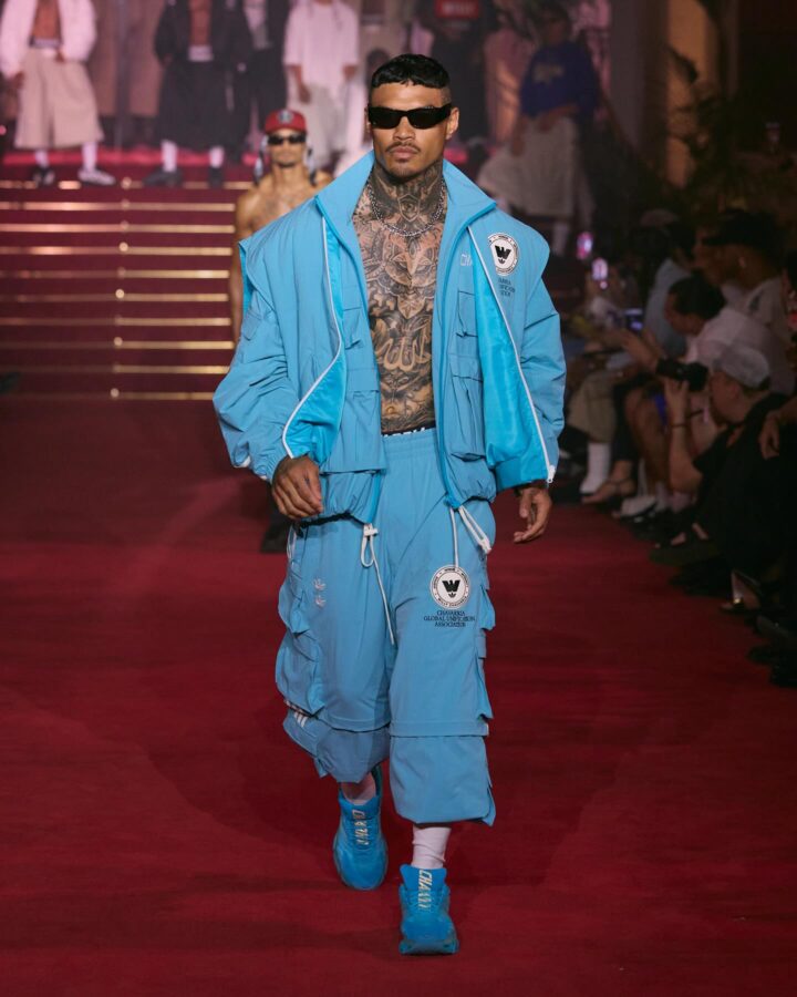 Total look en azul saturado de Willy Chavarria primavera/verano 2026: chándal cargo turquesa con parches de la Chavarria Global Unification Association y zapatillas a juego