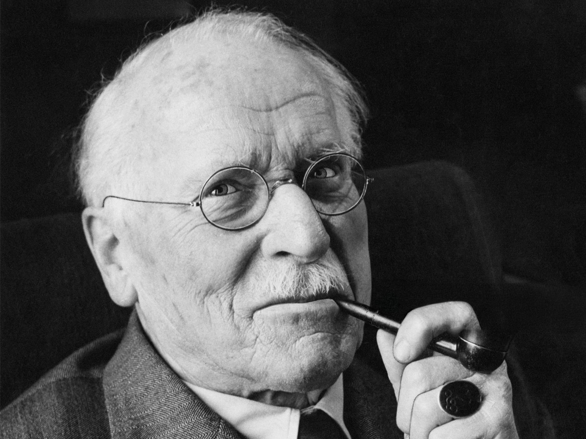 Primer plano en blanco y negro de Carl Gustav Jung con pipa, gafas redondas y un anillo en la mano.