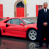 Así era la millonaria colección de coches de Lewis Hamilton que vendió para invertir en arte: desde un Shelby Cobra hasta un Pagani Zonda personalizado Lewis Hamilton vestido de traje con un coche rojo detrás