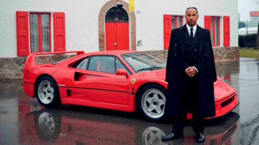Lewis Hamilton vestido de traje con un coche rojo detrás