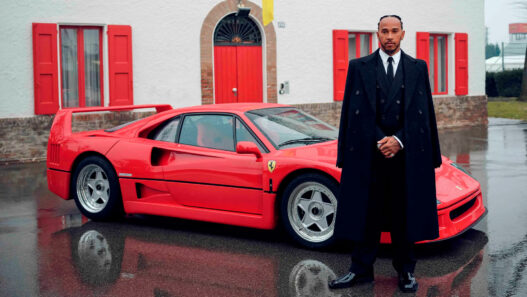Lewis Hamilton vestido de traje con un coche rojo detrás