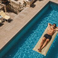 Los dermatólogos coinciden: "El daño solar que de verdad cuenta no es la quemadura de la playa" Hombre tumbado sobre una colchoneta en una piscina junto al mar, tomando el sol sin protección solar.