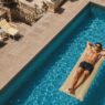 Hombre tumbado sobre una colchoneta en una piscina junto al mar, tomando el sol sin protección solar.