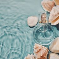 10 perfumes de hombre para el verano 2026 que se convertirán en tu nueva obsesión...¡olfativa! fraco de perfume sumergido en agua de mar con cochas al rededor.