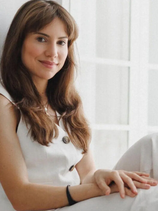 Isabel Viña, médica y divulgadora, sentada junto a una ventana con chaleco blanco
