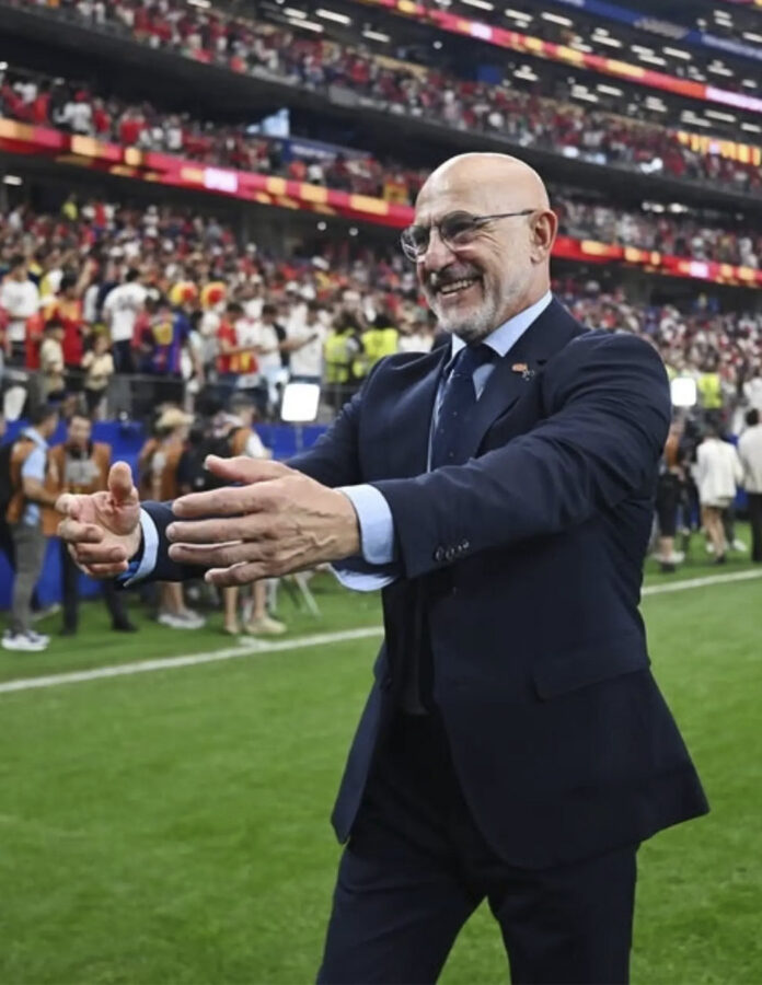 Luis de la Fuente con traje azul marino celebra sobre el césped en un estadio lleno