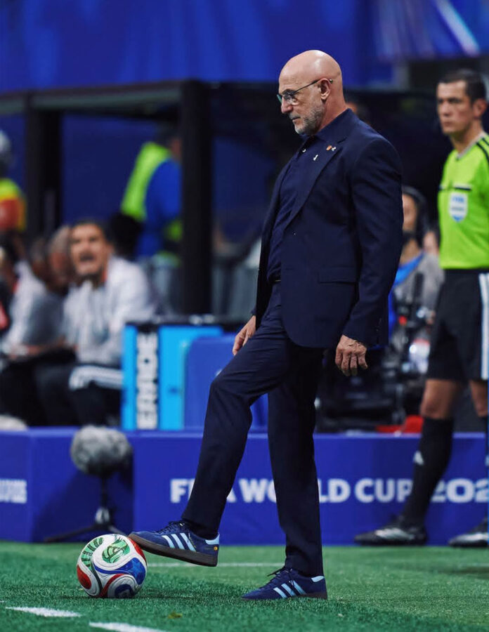 Luis de la Fuente con traje azul y zapatillas Adidas Spezial apoya el pie sobre el balón en el Mundial 2026