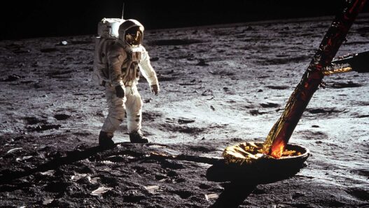 Astronauta del Apolo 11 caminando sobre la superficie lunar junto a la pata dorada del módulo lunar Eagle.