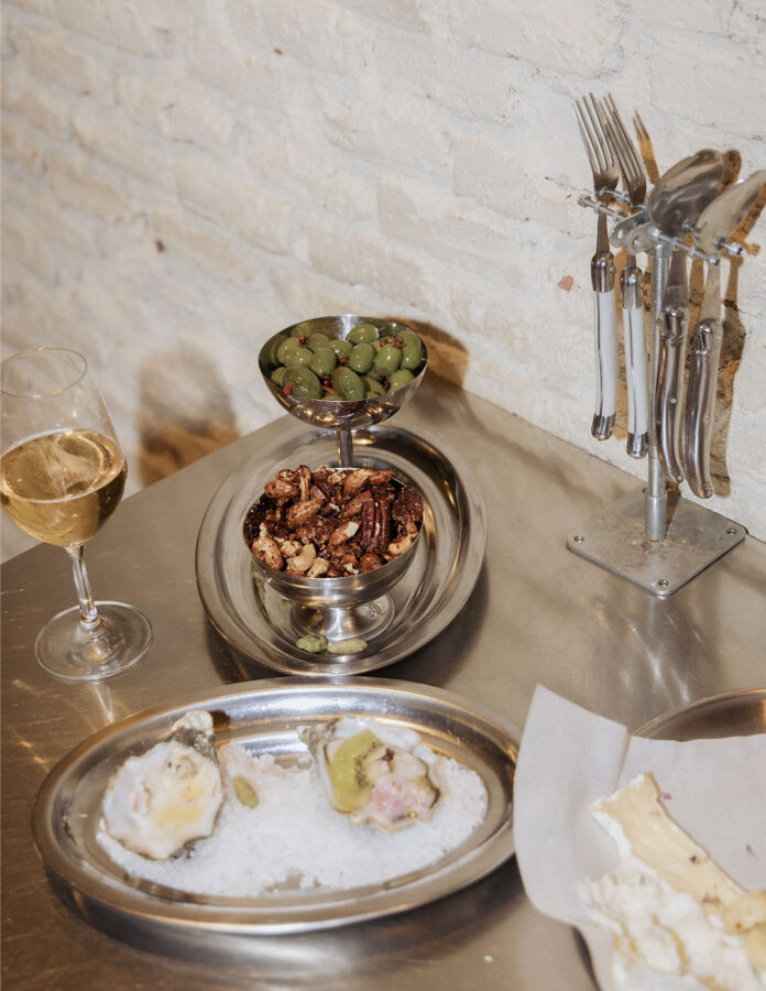 Ostras, aceitunas, frutos secos especiados y queso servidos con vino blanco en la cena de Scalpers en Masa Vins