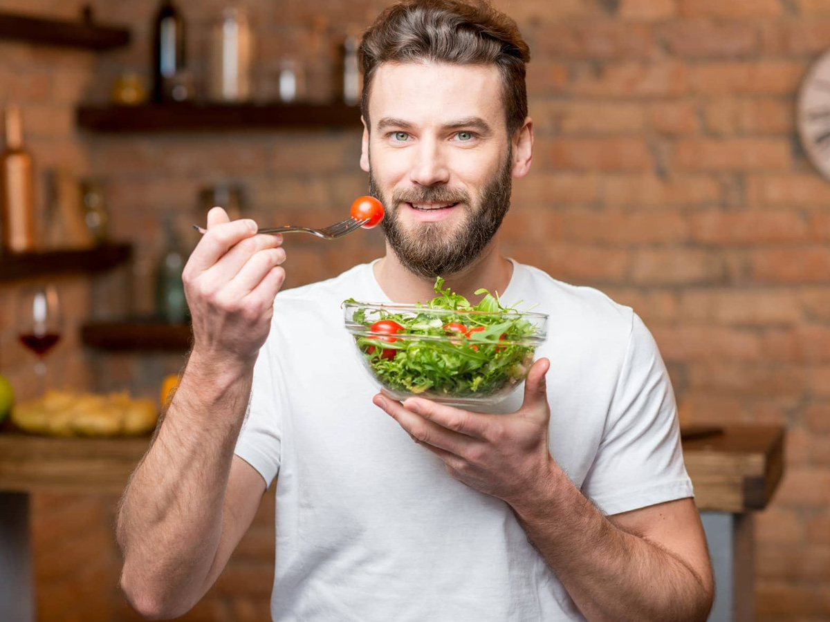 Hombre de 40 años comiendo una ensalada como parte de una dieta rica en proteína para frenar la pérdida de masa muscular