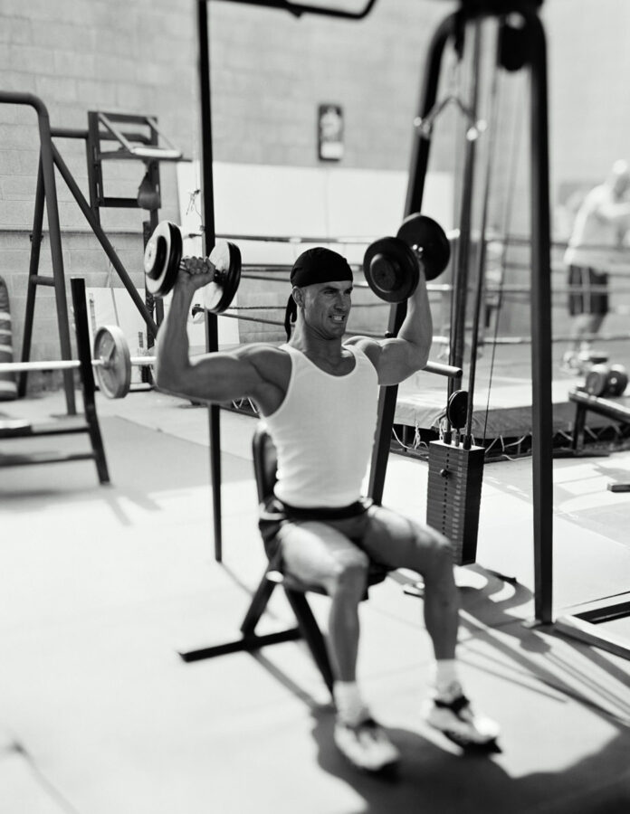 Hombre de más de 40 años entrenando press de hombro con mancuernas para prevenir la pérdida de masa muscular y potencia