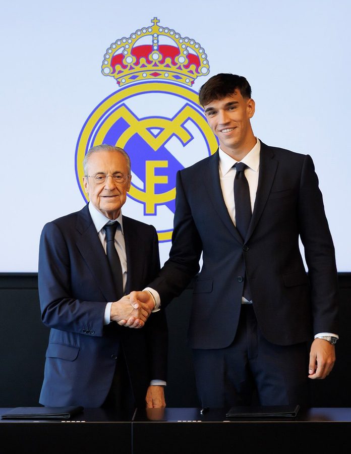 Carlos Espí estrecha la mano de Florentino Pérez con traje azul marino y corbata en su firma como jugador del Real Madrid