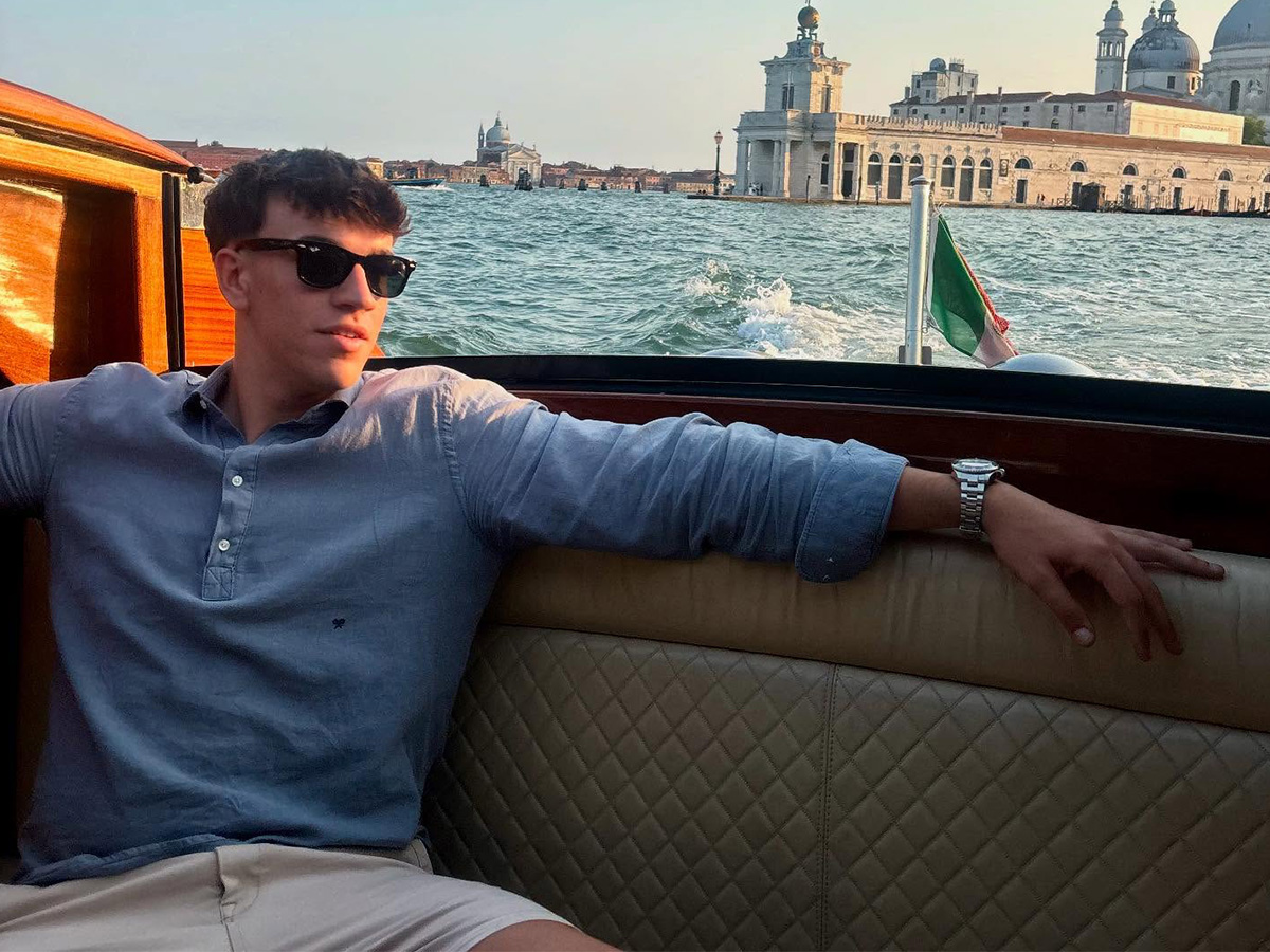 Carlos Espí con camisa polera azul de lino, bermudas beige y gafas de sol Ray-Ban en una lancha por los canales de Venecia