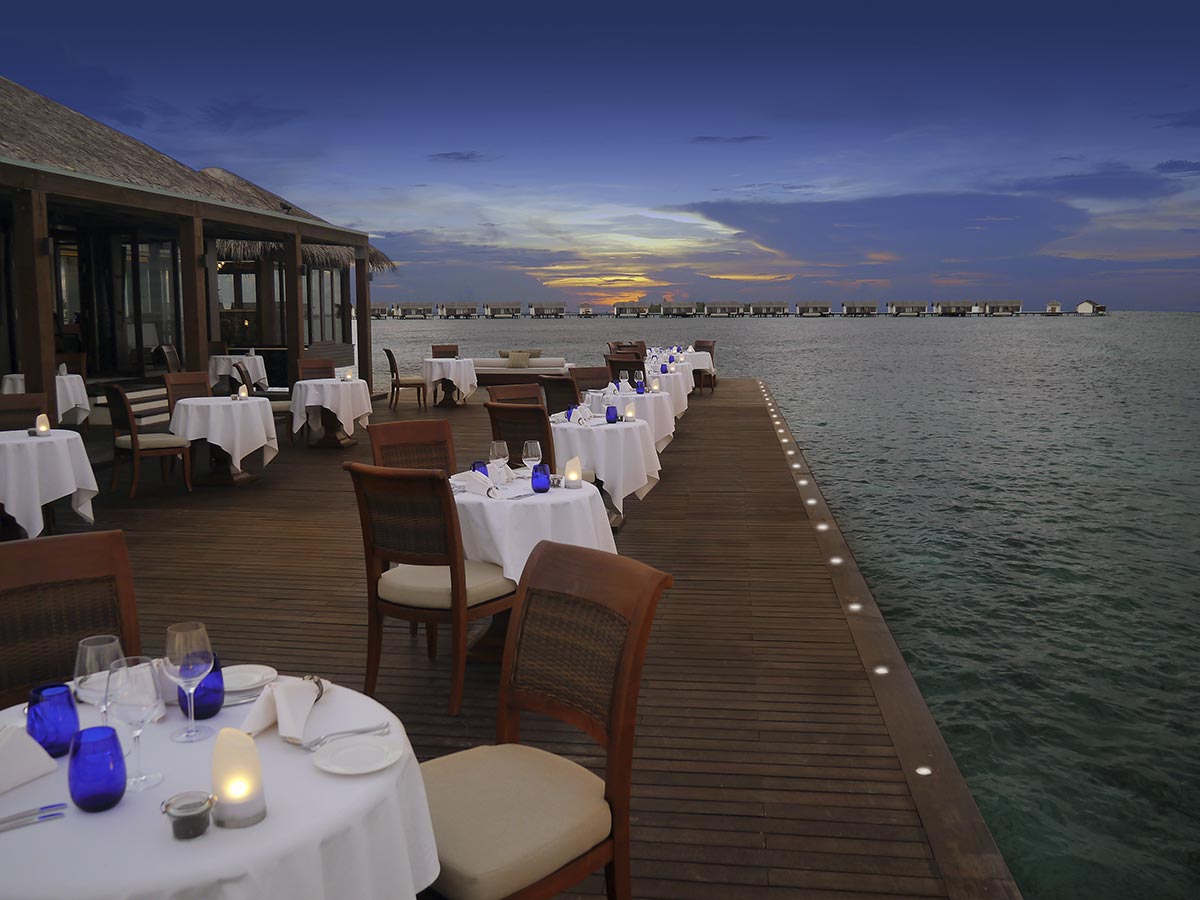 Restaurante sobre el agua del resort The Residence en Maldivas al atardecer