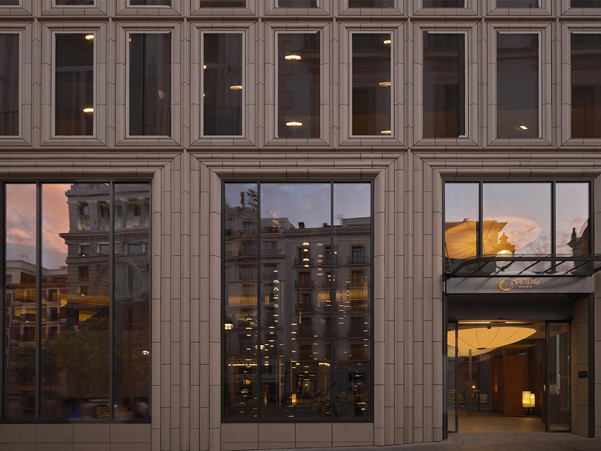 Fachada y entrada de Nobu Hotel Madrid al atardecer con los edificios de la calle Alcalá reflejados en sus ventanales