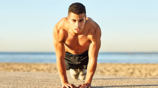 Hombre haciendo flexiones en la playa para entrenar el pectoral en verano sin material