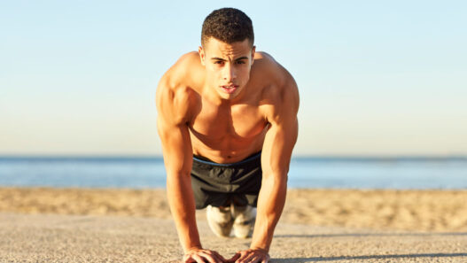 Hombre haciendo flexiones en la playa para entrenar el pectoral en verano sin material