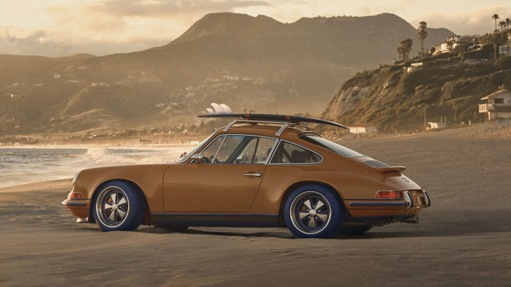 Vista lateral del Porsche 911 Reimagined by Singer y Louis Vuitton con tabla de surf en una playa de California