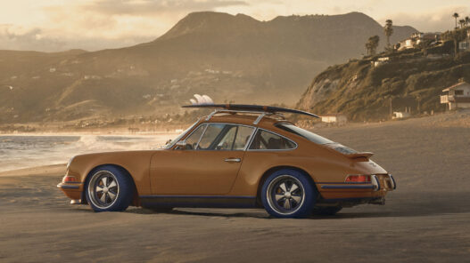 Vista lateral del Porsche 911 Reimagined by Singer y Louis Vuitton con tabla de surf en una playa de California