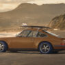 Vista lateral del Porsche 911 Reimagined by Singer y Louis Vuitton con tabla de surf en una playa de California