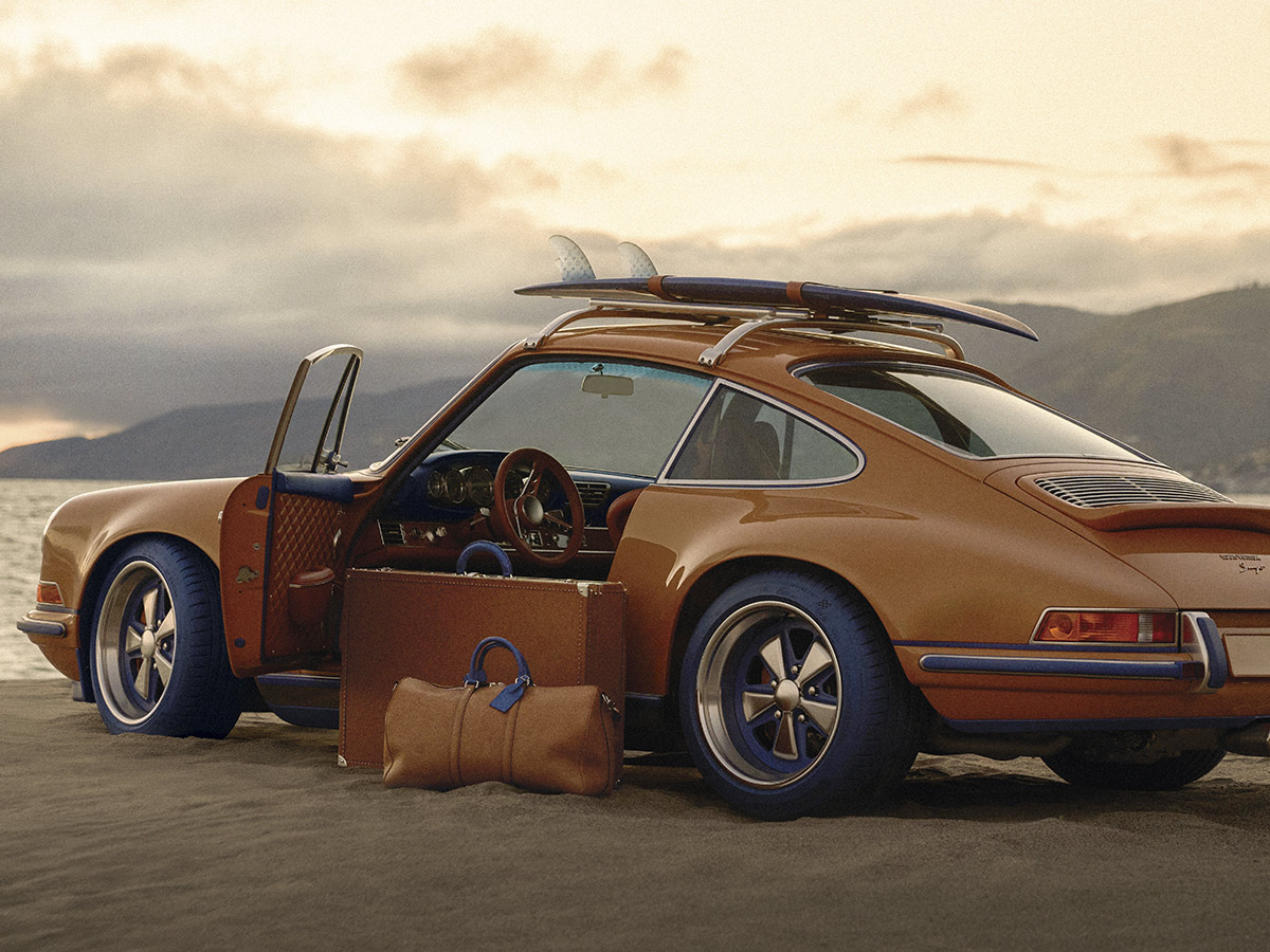 Porsche 911 Reimagined by Singer en color Saffron con tabla de surf y equipaje Louis Vuitton en la playa