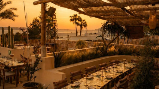 Terraza del restaurante Madunia en Ibiza al atardecer, con mesas bajo pérgola de madera y vistas al mar