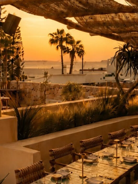 Terraza del restaurante Madunia en Ibiza al atardecer, con mesas bajo pérgola de madera y vistas al mar
