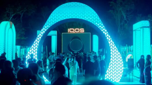 Arco luminoso de la House of IQOS con el logo IQOS en el centro y público bajando hacia el escenario de noche