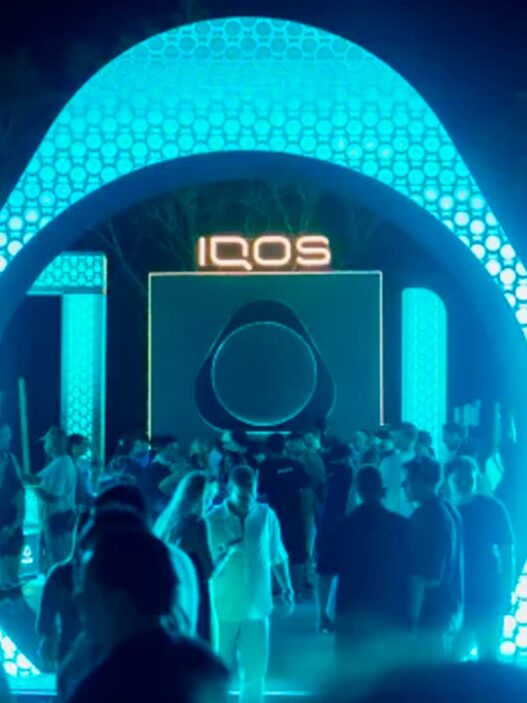 Arco luminoso de la House of IQOS con el logo IQOS en el centro y público bajando hacia el escenario de noche
